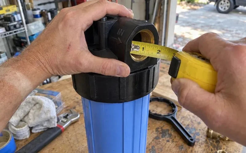 Hands measuring the threaded inlet port on a 10 inch filter housing cap