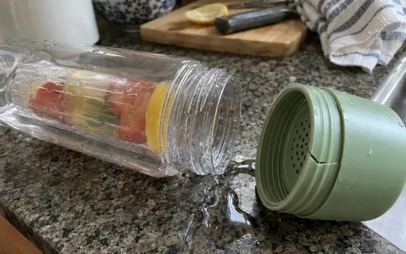 Plastic bottom-loading infuser base with a crack along its threads beside a small water puddle
