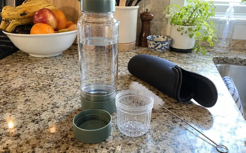 Bottom-loading infuser bottle with its insulating sleeve, unscrewed fruit cup and bottle brush