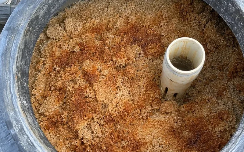Open sand filter tank showing filter sand stained orange-brown by iron buildup