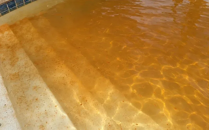 Close view of cloudy orange-brown pool water with rust-colored iron particles over a white pool floor